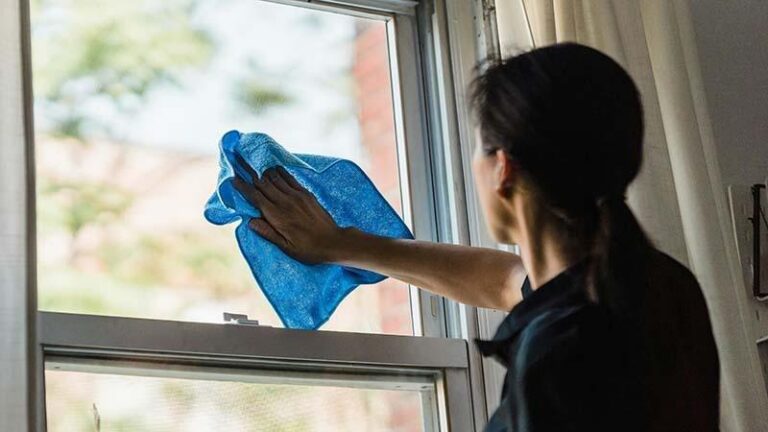 A woman cleaning her window with a blue microfiber cloth