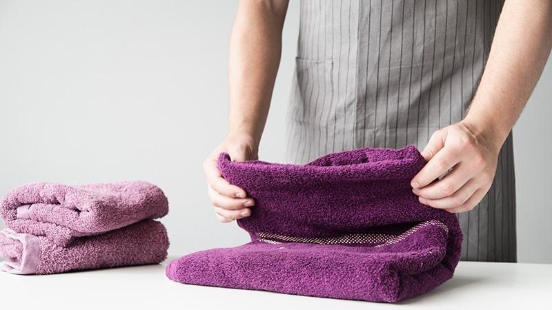 Man folding a purple high GSM towel
