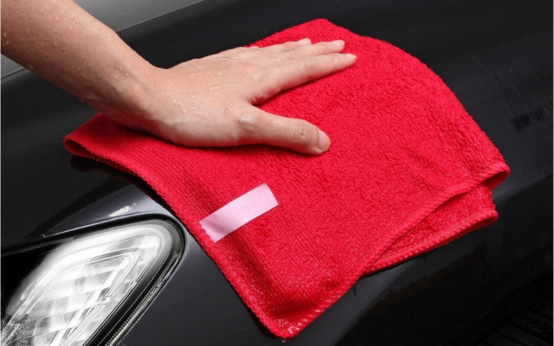 A man is wiping down his car with a red microfiber towel.