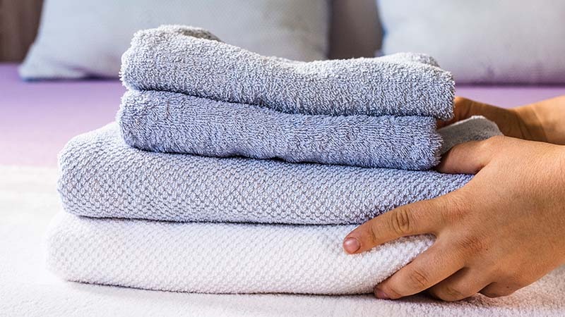 Housekeep placing microfiber towels on hotel bed
